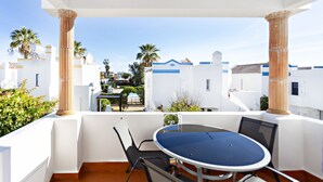 A terrace with a round table and chairs, overlooking a white building with blue accents and palm trees. - QV 14B - Casa da Pintora - Quinta Velha (Tavira)