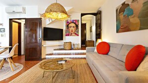 A living room with a sofa, a coffee table, a TV, and a painting on the wall. - QV 14B - Casa da Pintora - Quinta Velha (Tavira)