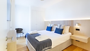 A modern bedroom with a large bed, bedside tables, a chair, and a wardrobe.