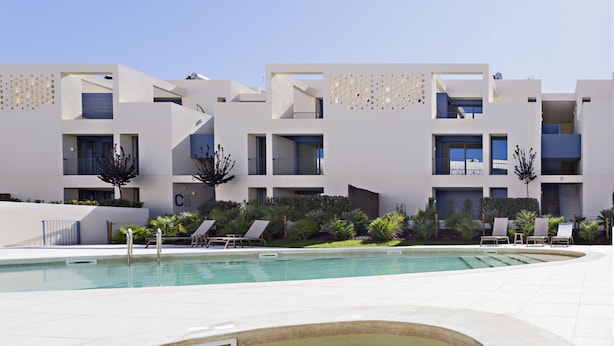 A modern hotel with a pool, multiple balconies, and a well-maintained garden.
