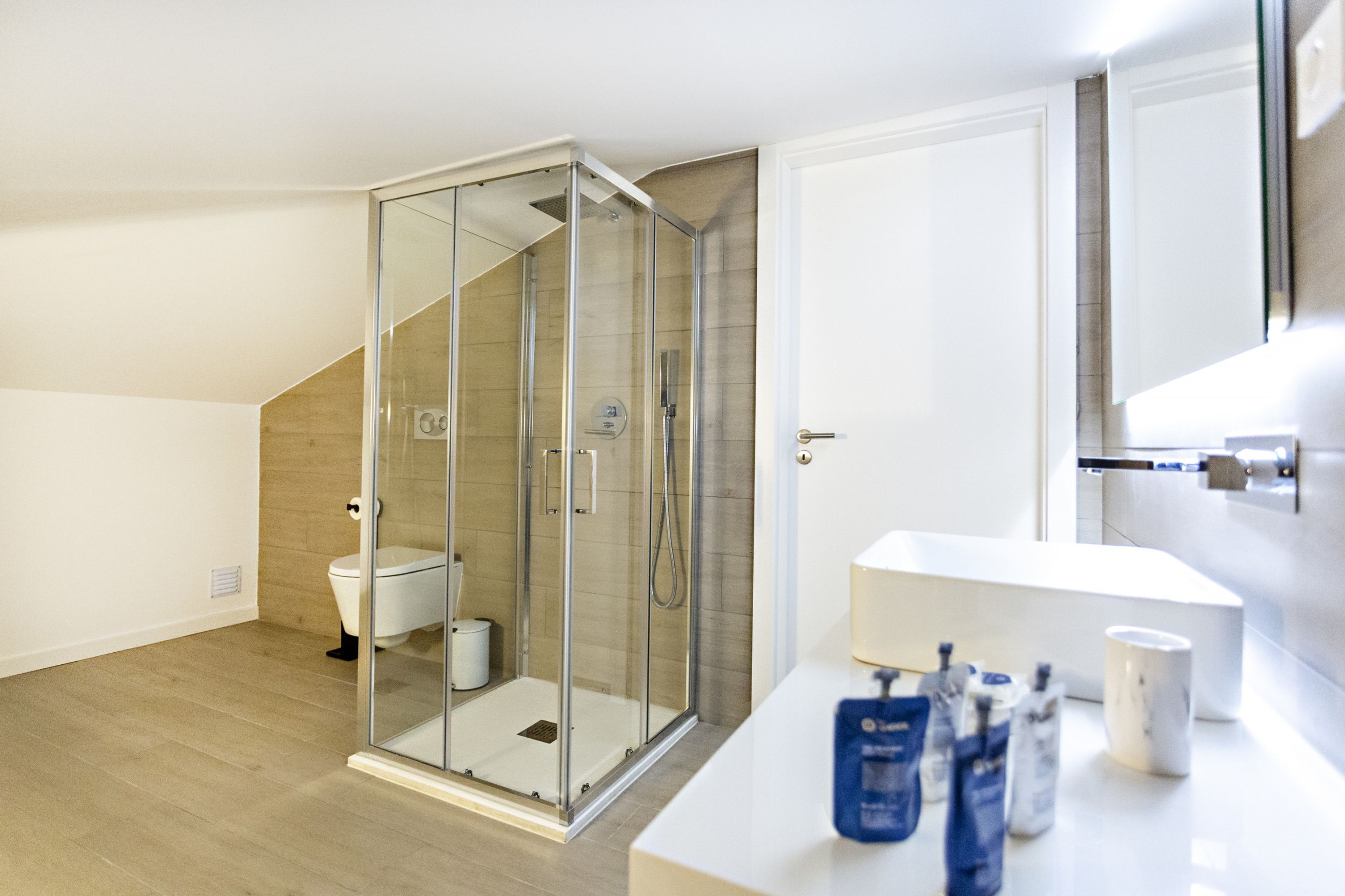 A modern bathroom with a glass-enclosed shower, a toilet, and a white sink with toiletries.