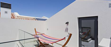 A balcony with a wooden hammock and a glass railing.