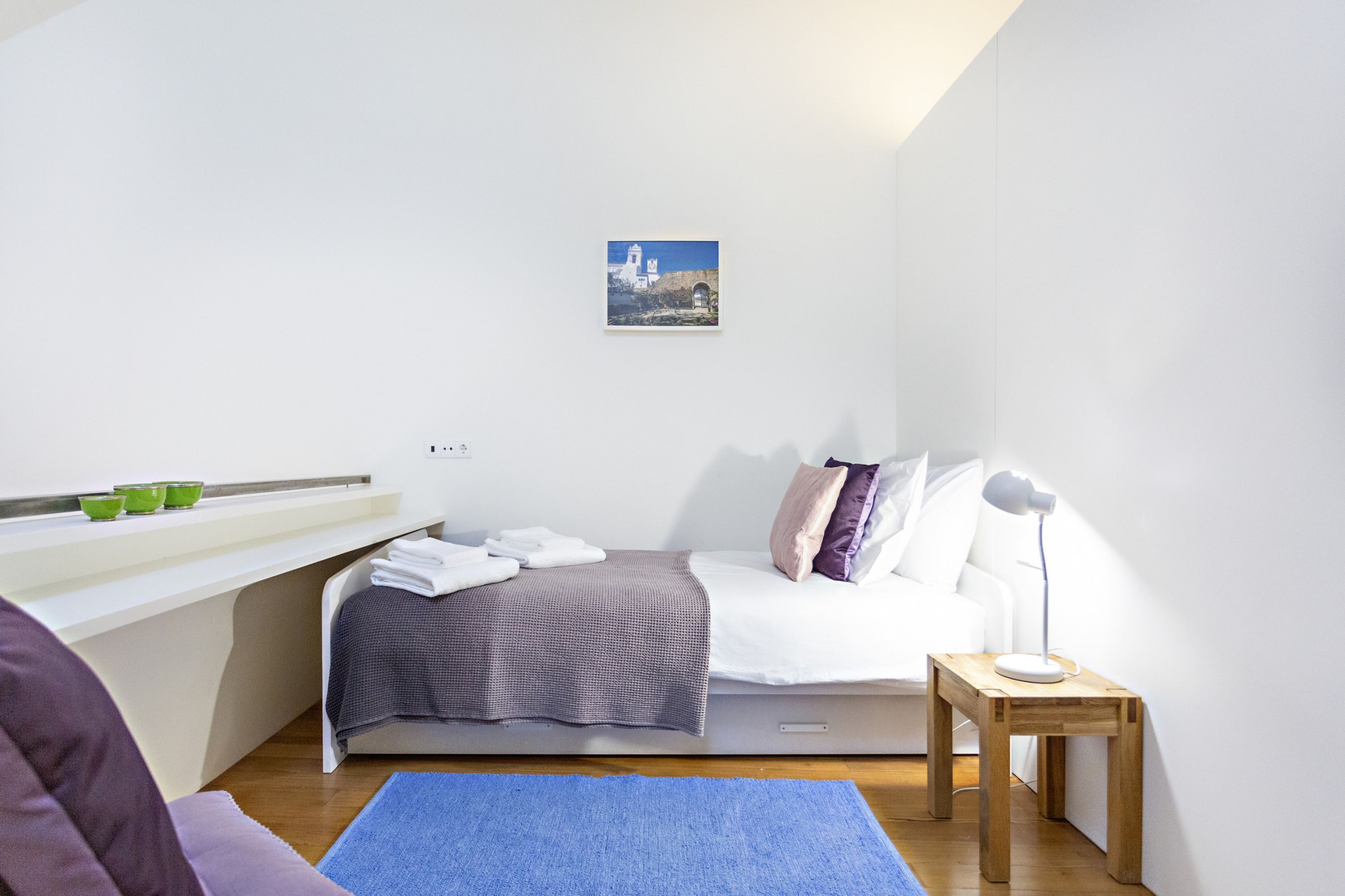 A modern bedroom with a bed, bedside table, lamp, and a small picture on the wall.