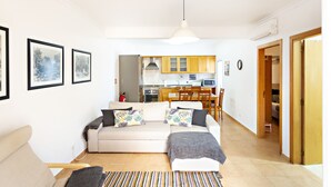 A living room with a sofa, a coffee table, and a striped rug. There is a kitchen in the background with wooden cabinets and a microwave. - Casa Correia in Vila Real de Santo Ant nio (Vila Real Santo Antonio)