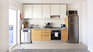 Una cocina moderna con armarios blancos, electrodomésticos de acero inoxidable y vistas de la ciudad a través de un ventanal amplio.