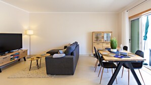 Una sala de estar moderna con sofá, televisión y comedor con sillas y mesa.