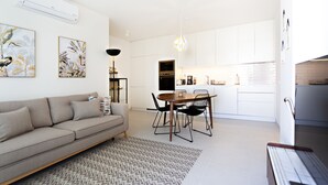 A modern living room with a sofa, dining table, and chairs, a kitchen area with cabinets and appliances, and a hanging light fixture. - Casas do Forte CG in Tavira (Tavira)