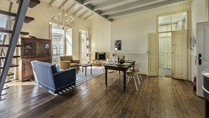 A spacious living room with wooden floors, a dining table, and a sofa. There is a staircase on the left and a door leading to another room. - Casa do Jornal in Vila Real de Santo Ant nio (Vila Real Santo Antonio)