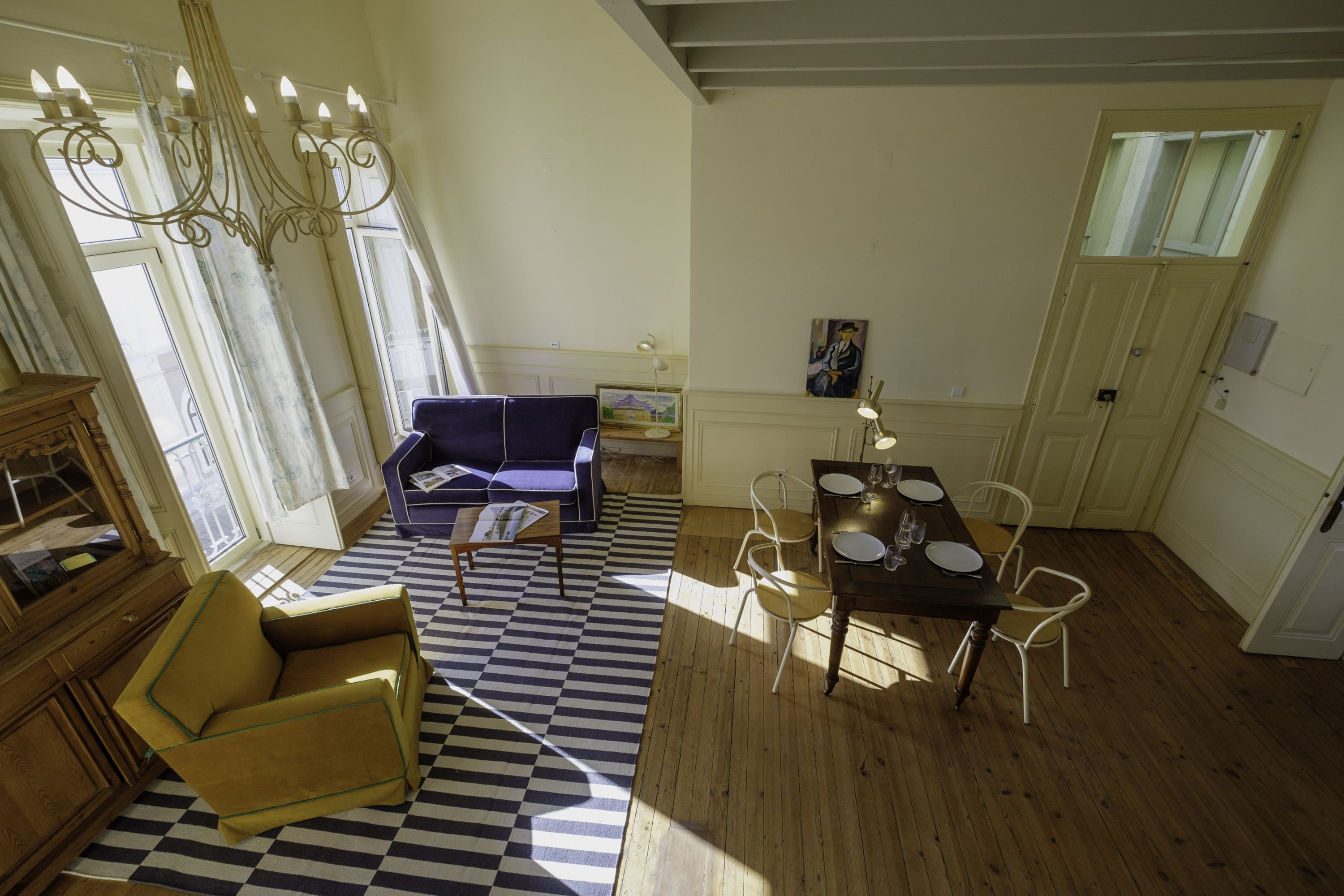 A room with a checkered floor, a dining table with chairs, a sofa, a wooden cabinet, and a chandelier.
