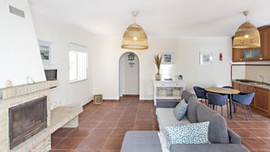 A spacious living area with a fireplace, a grey sofa with patterned cushions, a dining table with chairs, and a kitchen area with wooden cabinets. - Casa Santo in Tavira (Tavira)