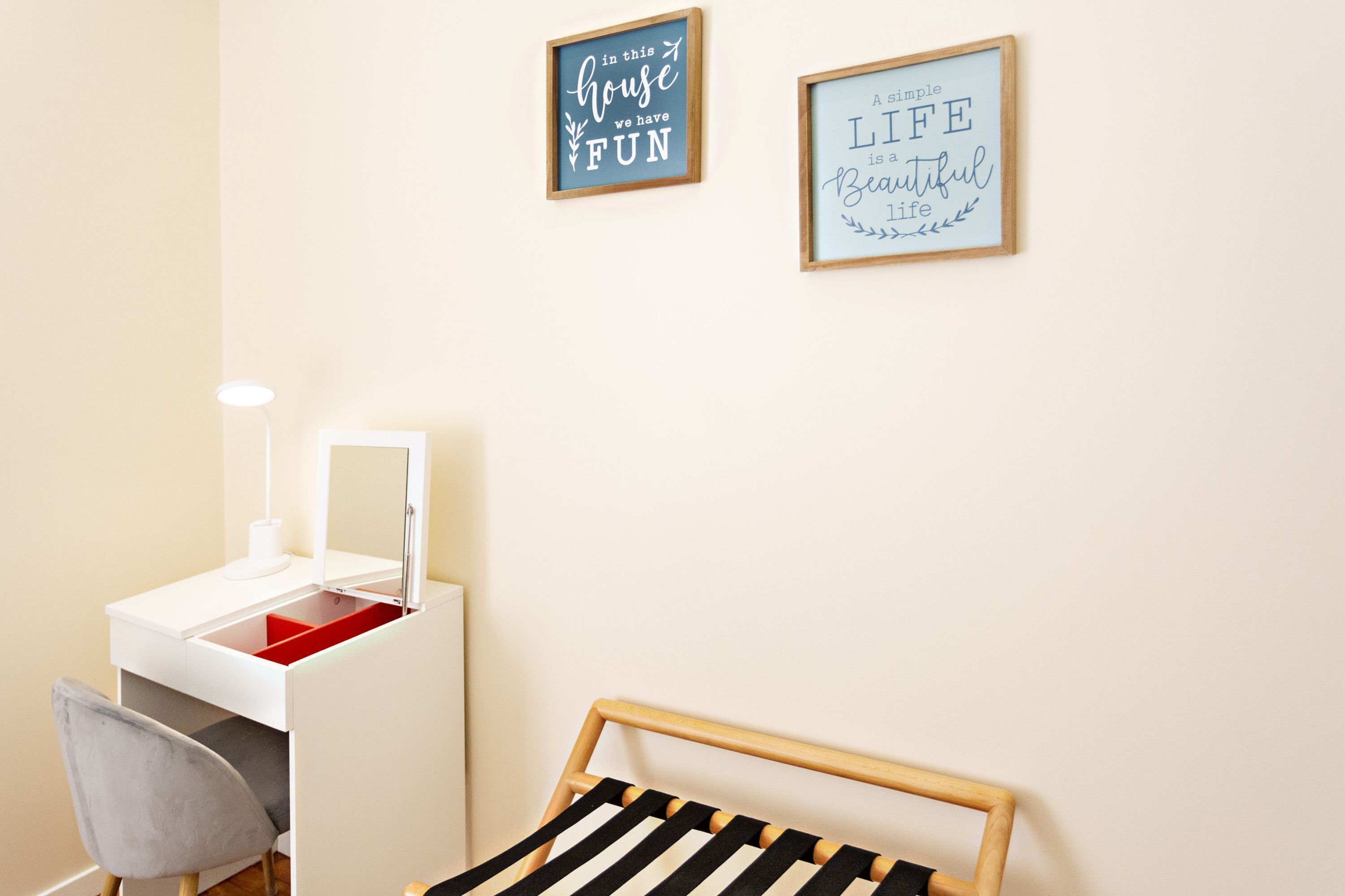 Una stanza con una toeletta, una sedia, un letto e due quadri con citazioni motivazionali appesi al muro.