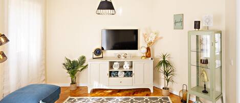 A living room with a TV, white cabinet, blue sofa, patterned rug, and decorative items.