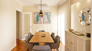 A dining area with a wooden table, six chairs, a pendant light, a decorative wall piece, and a cabinet with a mirror. - Blue Peacock in Faro (Faro)