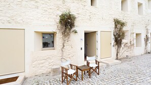 A building with a stone facade, a courtyard with a wooden table and chairs, and a door marked with an 'AL' sign. - CV BC - Convento das Bernardas (Tavira)