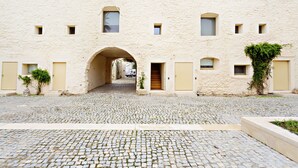 A cobblestone courtyard with a central archway leading to a building with multiple small windows and doors. - CV BC - Convento das Bernardas (Tavira)
