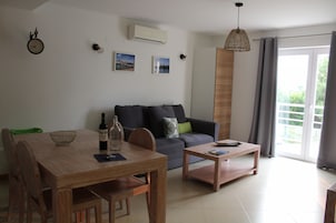 Una sala de estar moderna con una mesa de comedor de madera, un sofá gris y una mesa de centro. Hay un reloj en la pared y una ventana con cortinas.