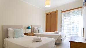 Une chambre d’hôtel avec deux lits, une armoire en bois, un bureau et une fenêtre avec des stores.