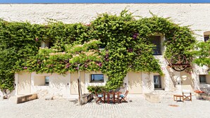 A building with a stone facade, a covered outdoor seating area with a table and chairs, and a staircase leading to an upper level. - CV P- Convento das Bernardas (Tavira)