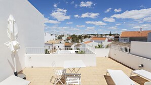 Una terraza en la azotea con mobiliario blanco, que incluye una mesa y sillas, y una sombrilla blanca.