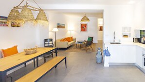 Una cocina moderna con armarios blancos, una mesa de comedor de madera y un banco. Hay una lámpara colgante sobre la mesa.