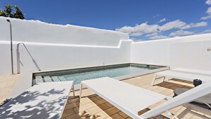 Zona de piscina con sillas reclinables blancas y un cielo azul despejado.