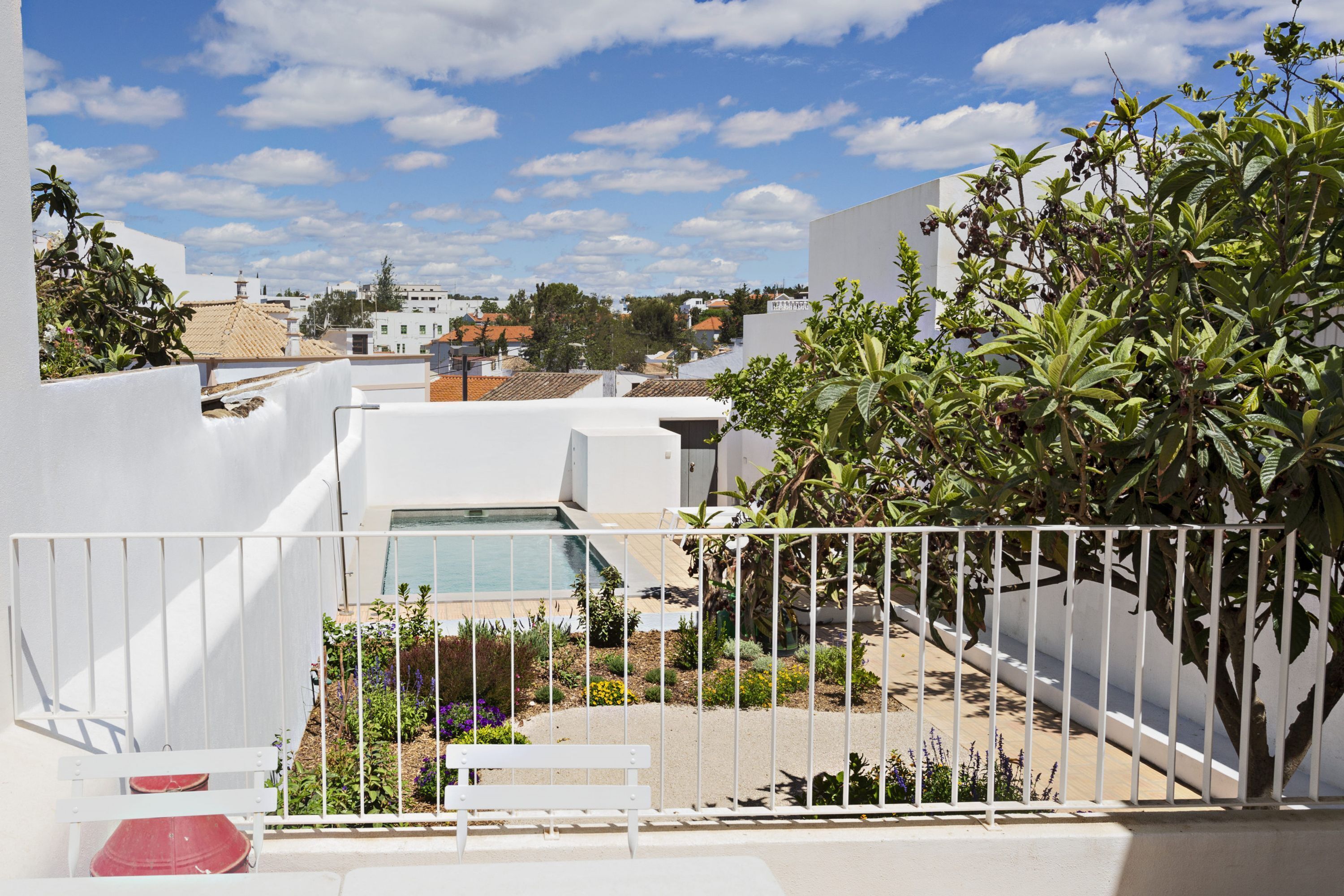 Une terrasse sur le toit avec une piscine, entourée de murs blancs et de verdure.