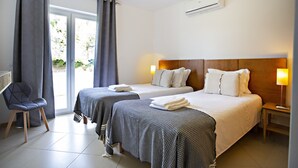 A hotel room with two beds, a chair, and a window with curtains.
