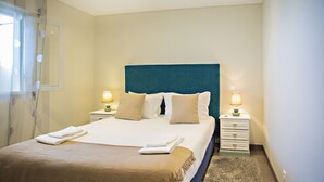 A neatly made bed with a blue headboard, two bedside tables with lamps, and a small rug.