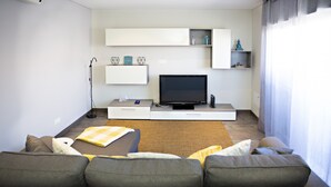 A modern living room with a grey sofa, a flat-screen TV, and built-in shelving.