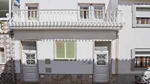 A two-story building with a balcony, two windows with metal grilles, and a door. - Talabriga - Apt Cidade (Tavira)