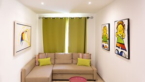 A living room with a beige sectional sofa, green curtains, and two framed artworks on the walls. - Talabriga - Apt Cidade (Tavira)