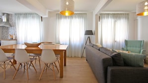 Una sala de estar moderna con comedor, que incluye un sofá, sillas, una mesa y luminarias colgantes.