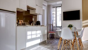 Eine moderne Küche mit weißen Schränken, ein Essbereich mit weißen Stühlen und ein flachbildfernseher an der Wand.