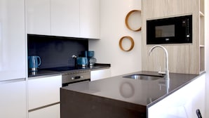 A modern kitchen with white cabinets, a built-in microwave, a coffee maker, and a stainless steel sink.
