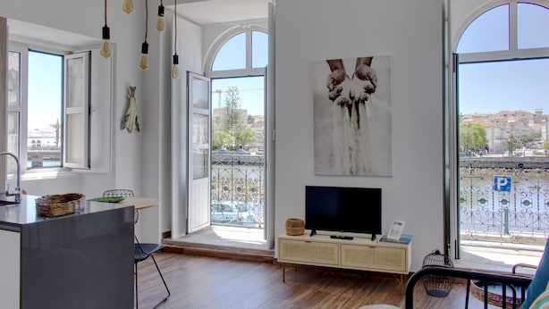 A modern living room with a large TV, open windows, and a balcony with a city view.