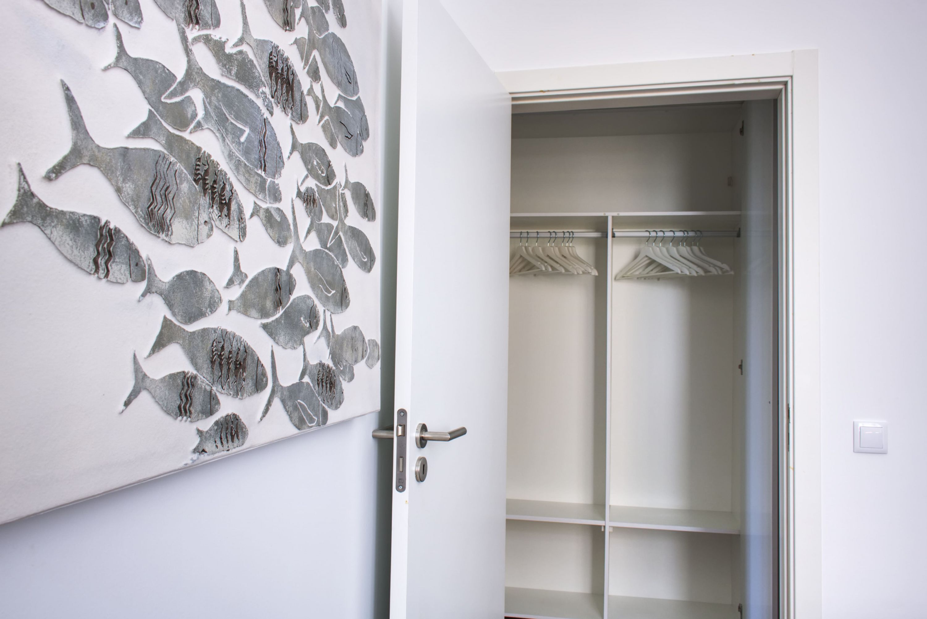 Une pièce avec une porte blanche, une décoration murale représentant des poissons et un placard partiellement visible, dans lequel on peut apercevoir des vêtements suspendus.