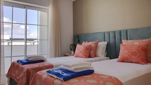 A hotel room with two beds, each with a patterned bedspread, a nightstand with a lamp, and a view of the sky through large windows. - Formosa Bay - HB in Tavira (Tavira)
