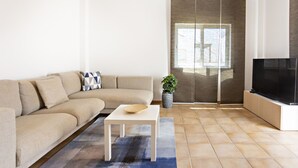 A modern living room with a beige sofa, a white coffee table, a TV, and a large window. - Cabanas Terrace in Tavira (Tavira)