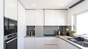 A modern kitchen with white cabinets, a built-in oven, a coffee machine, and a window with a view. - Cabanas Terrace in Tavira (Tavira)