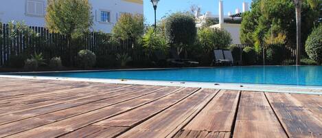 A wooden deck leading to a swimming pool with lounge chairs and a fence.