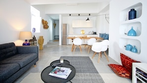 A modern living room with a grey sofa, a black coffee table with magazines, and a dining area with white chairs and a wooden table. - Casa Dona Ana in Tavira (Tavira)