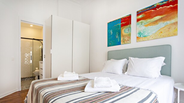 Ein Hotelzimmer mit einem großen Bett, weißen Leinen, einem gestreiften Teppich und zwei abstrakten Bildern an der Wand.