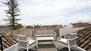 Eine Dachterrasse mit weißer Möbel, einer Fliesenwand und Blick auf die Stadtlandschaft.
