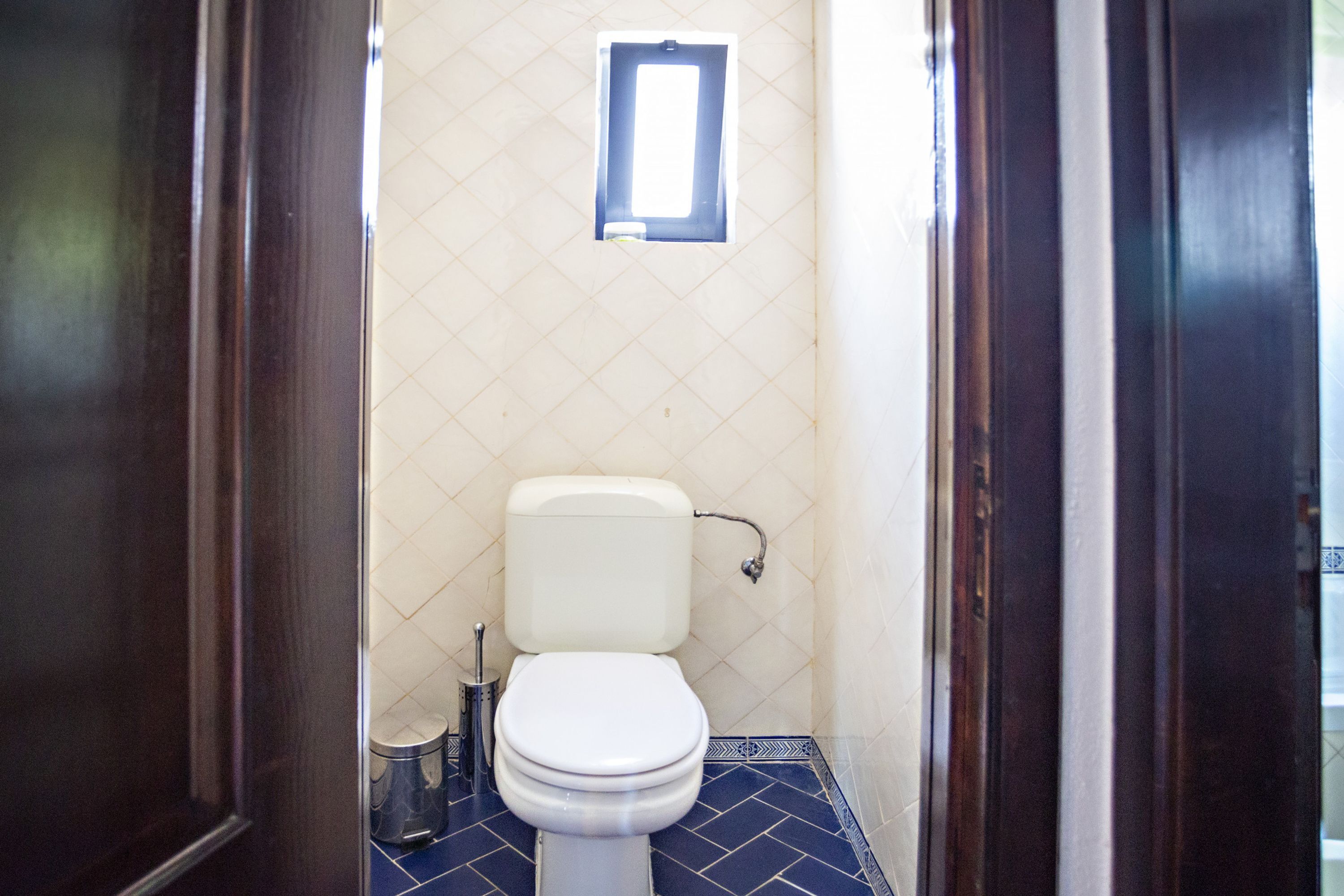 Une salle de bain avec des toilettes blanches, une petite fenêtre et un sol carrelé.