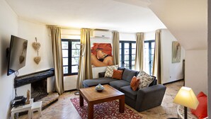 A living room with a fireplace, a sofa, a coffee table, and a TV mounted on the wall. - QV 4 - Villa Rustique - Quinta Velha (Tavira)