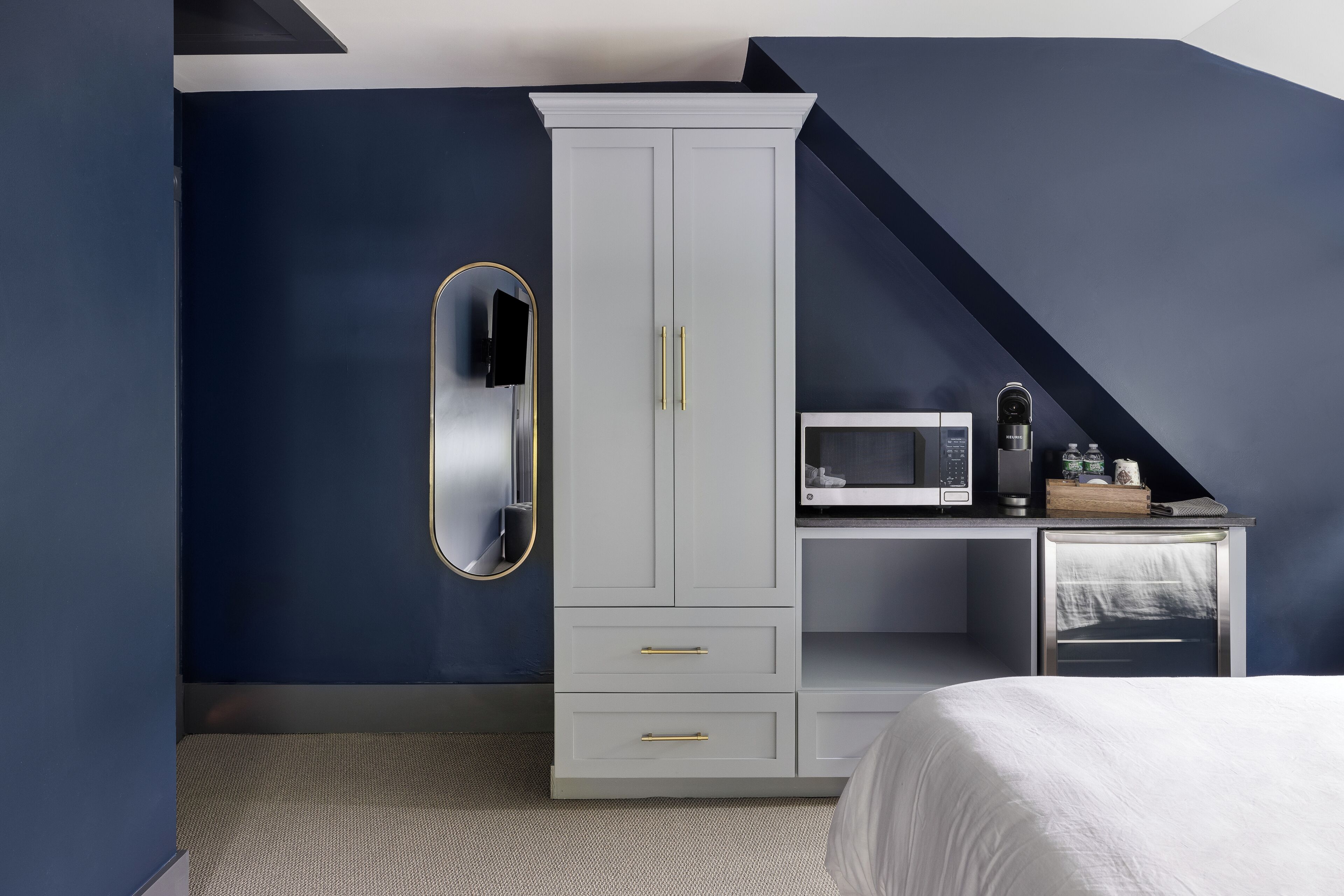 Une chambre avec une armoire blanche, un lit, un petit bureau avec un micro-ondes et une télévision.