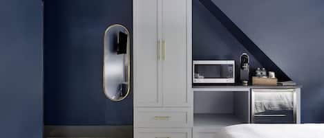 Une chambre avec une armoire blanche, un lit, un petit bureau avec un micro-ondes et une télévision.