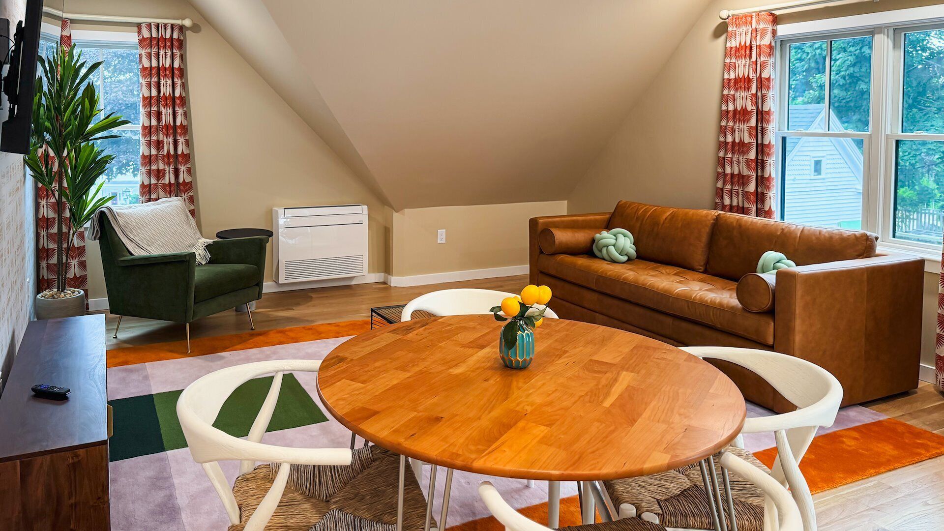 A cozy living room with a brown leather sofa, a green armchair, and a round wooden table with a vase of flowers.