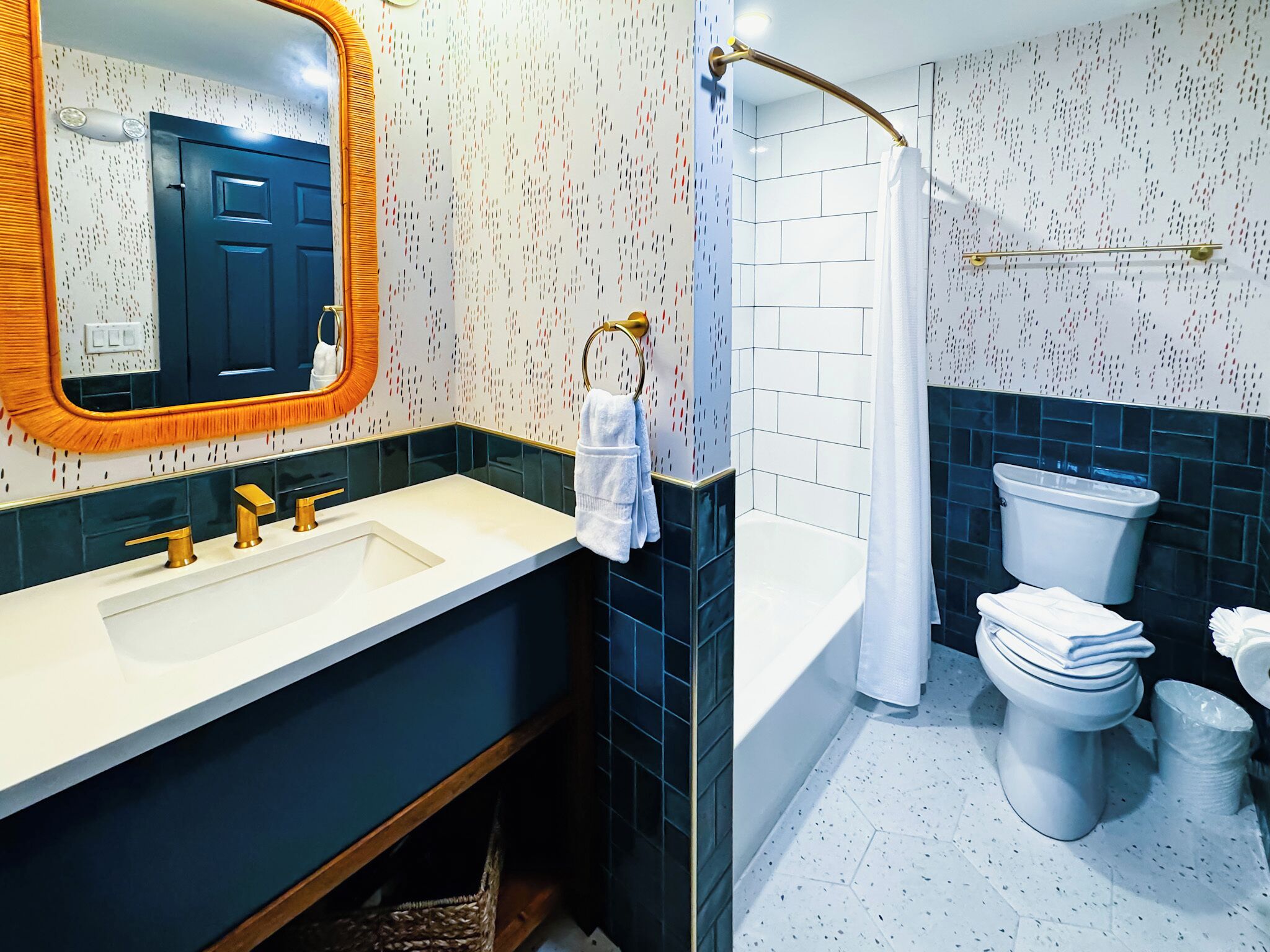 A modern bathroom with a white sink, gold fixtures, a large mirror, a shower with a glass door, and a toilet with a paper towel holder.