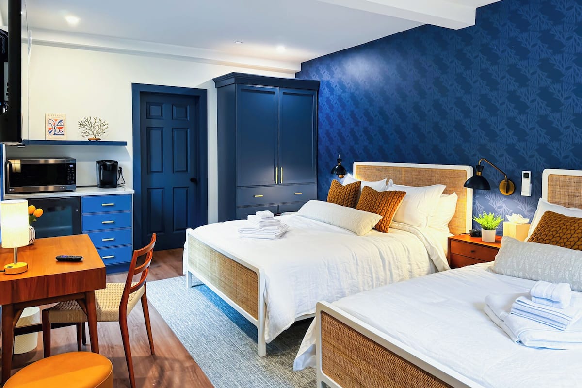 Une chambre d’hôtel comprenant un lit, des tables de chevet, un bureau, une chaise, une armoire et une kitchenette.